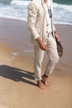 a man standing on top of a sandy beach next to the ocean with his hands in his pockets