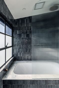 a bath tub sitting under a window next to a tiled bathroom wall with a shower head