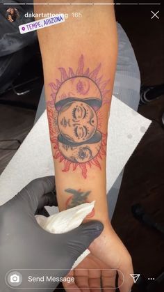 a person with a tattoo on their arm holding something in front of her face and the sun behind them