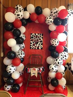 a chair sitting in front of a red door surrounded by black, white and red balloons