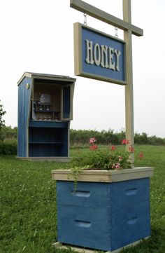 a blue beehive sitting in the grass next to a sign that says honey