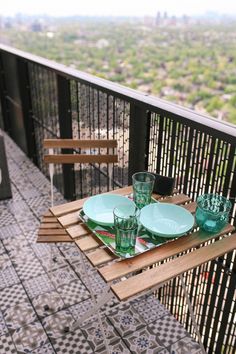 the table is set on the balcony with green plates and glasses in front of it