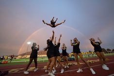 a group of cheerleaders standing on top of a track under a rainbow