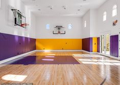 an indoor basketball court with purple and yellow painted on the walls, hardwood flooring