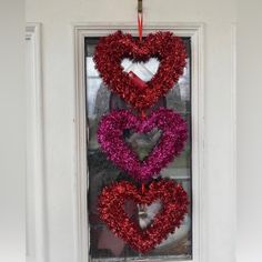 three heart shaped wreaths hanging on the front door with red and pink tinsel