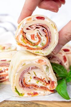 a person is holding a wrap with meat and cheese in it on top of some green leaves