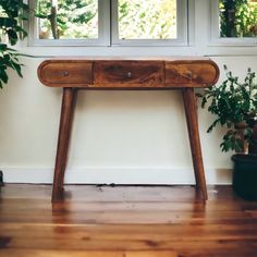 a wooden table sitting in front of a window next to a potted plant on top of a hard wood floor