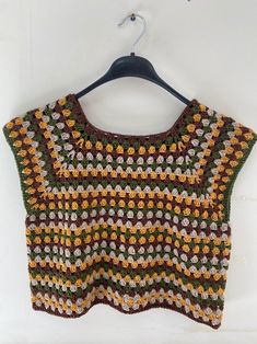 a crocheted sweater hanging on a hanger next to a white wall with an orange, yellow and green design