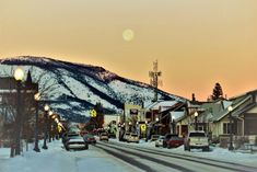 cars are parked on the side of a snowy road in front of buildings and mountains