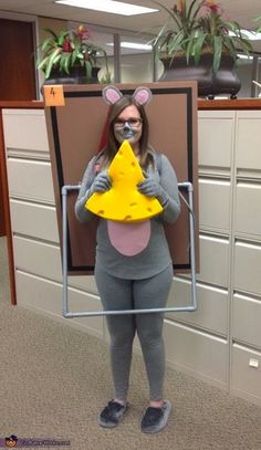 a woman dressed as a mouse holding a piece of cheese in front of her face