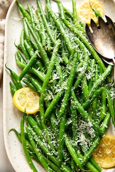 green beans with lemon slices and parmesan cheese on a white plate next to a spoon