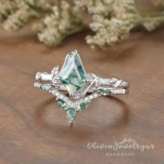 an engagement ring with green and white stones in the center on top of a wooden table