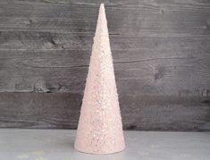 a pink glitter cone shaped christmas tree sitting on top of a wooden table next to a wall