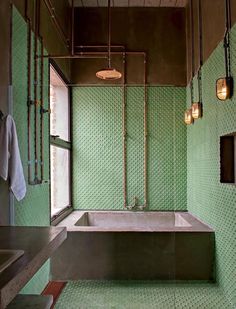 a bathroom with green tiled walls and a bathtub next to a sink under three lights