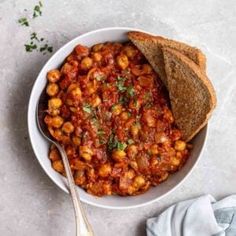 a white bowl filled with chickpeas and bread on top of a gray table