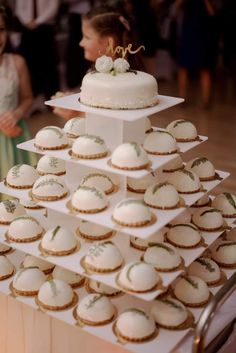 a white wedding cake and cupcakes on a table with people in the background