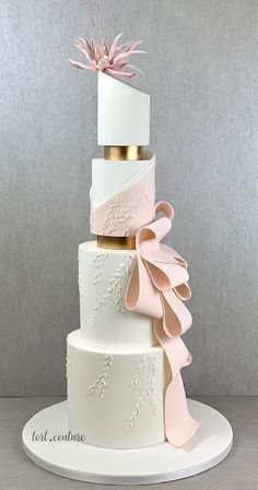 a three tiered wedding cake with pink ribbons and bows on the top, sitting on a white plate