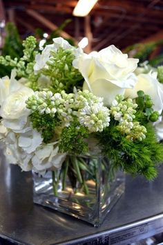 a clear vase filled with white flowers on top of a metal table covered in greenery