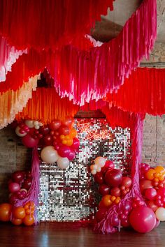 red, orange and pink decorations hanging from the ceiling in front of a brick wall