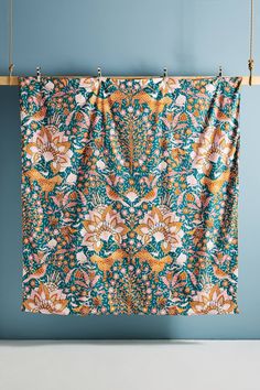 an orange and blue floral print curtain hanging on a clothes line against a blue wall