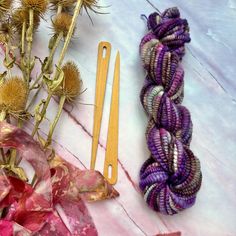 two skeins of yarn next to some flowers and a pair of knitting needles