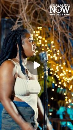 a woman singing into a microphone in front of a christmas tree with lights on it