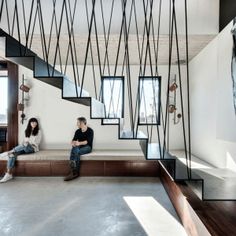 two people are sitting on a bench in the middle of a room with stairs and bookshelves