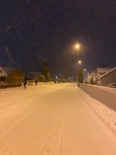 two people walking down a snow covered road at night with street lights in the distance