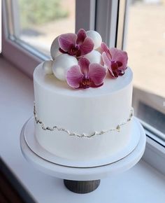 a white cake with pink orchids on top sitting in front of a window sill