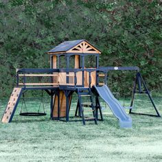 a wooden playset with a blue slide and green grass in front of some trees