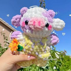 a hand holding a small crocheted sheep with flowers in it's mouth