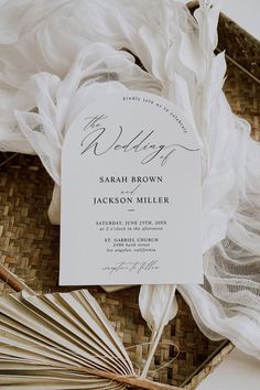 the wedding stationery is laid out on a wicker basket with an umbrella and fan