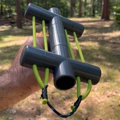 a hand holding an object in the middle of a forest with green cords attached to it