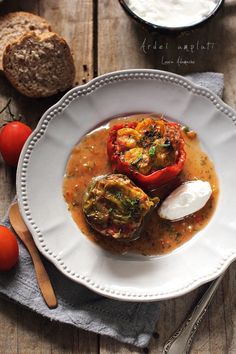 a white plate topped with food next to some bread and tomatos on top of a wooden table