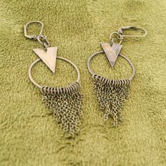 These fun geometric charm earrings come in a subtle antique brass finish. Each earring has a cascade of dainty chains hanging from a hoop in a chainmail reminiscent pattern. These bold and lively earrings are sure to make an impression. With a matching necklace available, this would make a fabulous gift set! -Geometric triangle and hoop charm -hanging chain accents -Antique brass finish -Leverback earring closure Handmade Geometric Brass Jewelry, Nickel-free Geometric Brass Earrings, Vintage Brass Dangle Hoop Earrings, Bronze Nickel-free Chandelier Earrings In Brass, Bronze Nickel-free Brass Chandelier Earrings, Brass Dangling Charms Drop Earrings, Nickel-free Bronze Dangle Hoop Earrings, Bronze Nickel-free Dangle Hoop Earrings, Minimalist Metal Dangle Chandelier Earrings