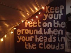 a man standing in front of a sign that says keep your feet on the ground when your heads in the clouds