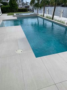 an empty swimming pool surrounded by palm trees and water in front of a large body of water