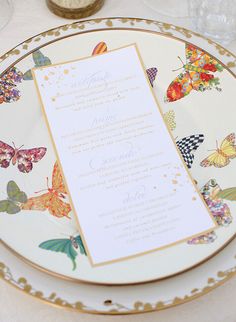 a wedding menu on a fancy plate with gold trimmings and colorful butterflies around it