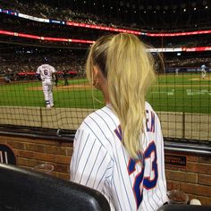 a woman sitting in the bleachers at a baseball game looking out into the stands