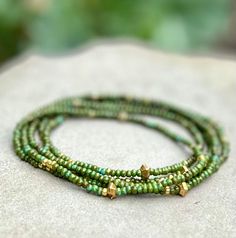 Made from speckled hunter-green Czech glass seed beads on strong elastic cording, these stretch bracelets wrap around your wrist five times and feature sprinkles of different-sized metallic gold beads throughout for a casual, yet elegant Boho style. Or mix with a creamy white and gold sprinkled 3- or 5-wrap for a free-spirited layered look. Made up of two separate wrap bracelets, these can be worn together or on their own, depending on your mood and style preference.​, and can also go twice arou Green Beaded Bracelet With Gold Beads, Green Bohemian Stretch Bracelet With Faceted Beads, Adjustable Green Beaded Bracelets With Gold Beads, Green Multi-strand Beaded Bracelets With Faceted Beads, Gold Spiritual Wrap Bracelet With Colorful Beads, Spiritual Gold Wrap Bracelet With Colorful Beads, Green Multi-strand Hand-strung Bracelets, Bohemian Green Beaded Bracelets With Gold Beads, Adjustable Green Bracelets With Gold Beads