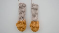 two crocheted oven mitts hanging from strings on a white surface with yellow and gray yarn