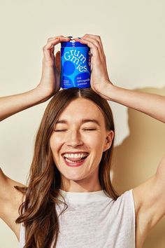 a smiling woman holding up a can of pure blue water to her head with both hands