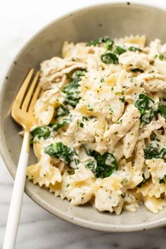 a white bowl filled with pasta and spinach covered in chicken sauce next to a fork