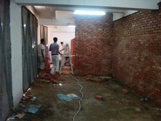 three men are standing in an unfinished room with brick walls and exposed pipes on the floor