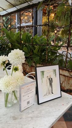 two vases filled with white flowers sitting on top of a table next to pictures