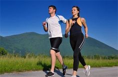 a man and woman running down the road in front of some green hills on a sunny day