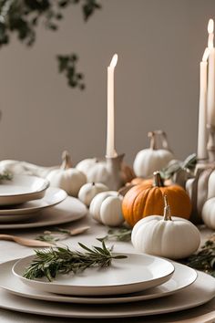 the table is set with white plates and pumpkins, candles and greenery on it