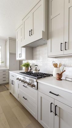 a kitchen with white cabinets and an oven in the center is seen from across the room