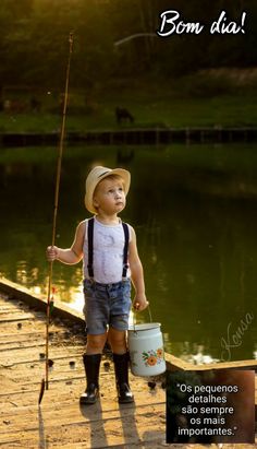 a young boy holding a fishing pole and bucket while standing on a dock next to a lake