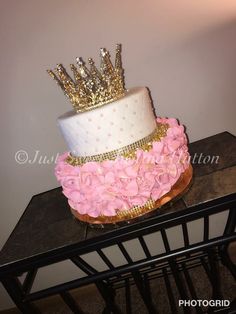 a white cake with pink flowers and a gold crown on top is sitting on a table